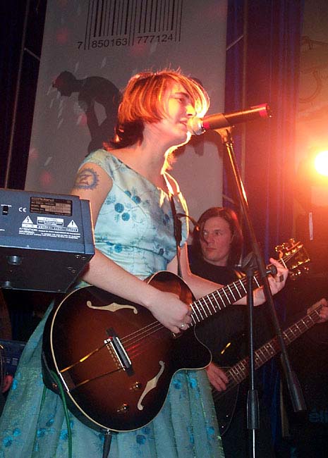 Земфира поёт с акустической гитарой в голубом платье и с татуировкой Z на правой руке